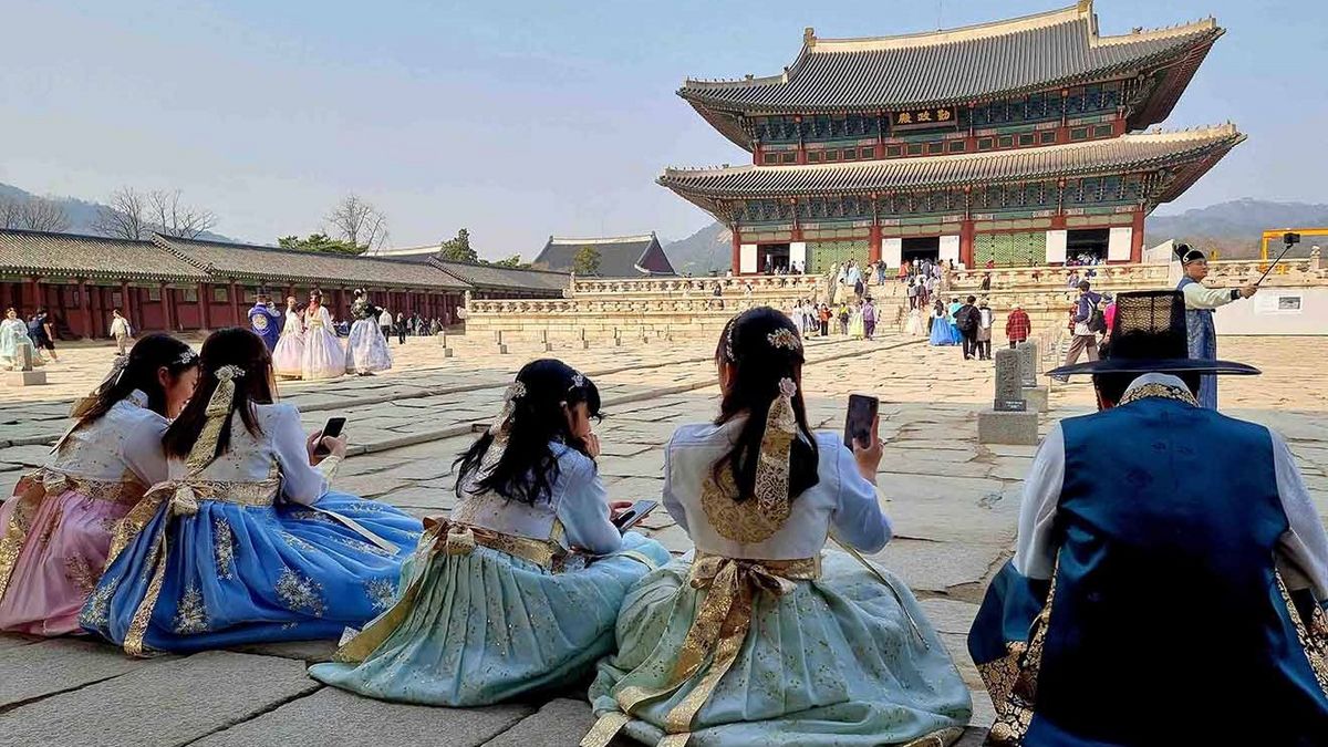 Eine Gruppe von Menschen in Hanboks vor dem Gyeongbokgung Palast in Seoul. Frauen sitzen auf dem Hof und machen Fotos