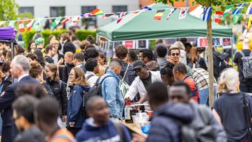 Das Bild zeigt Besucherinnen und Besucher des Internationalen Sommerfestes. Sie laufen umher, stehen an den Ständen, unterhalten sich oder essen und trinken. Über dem Platz ist eine Kette mit unterschiedlichen Landesflaggen aufgehängt.