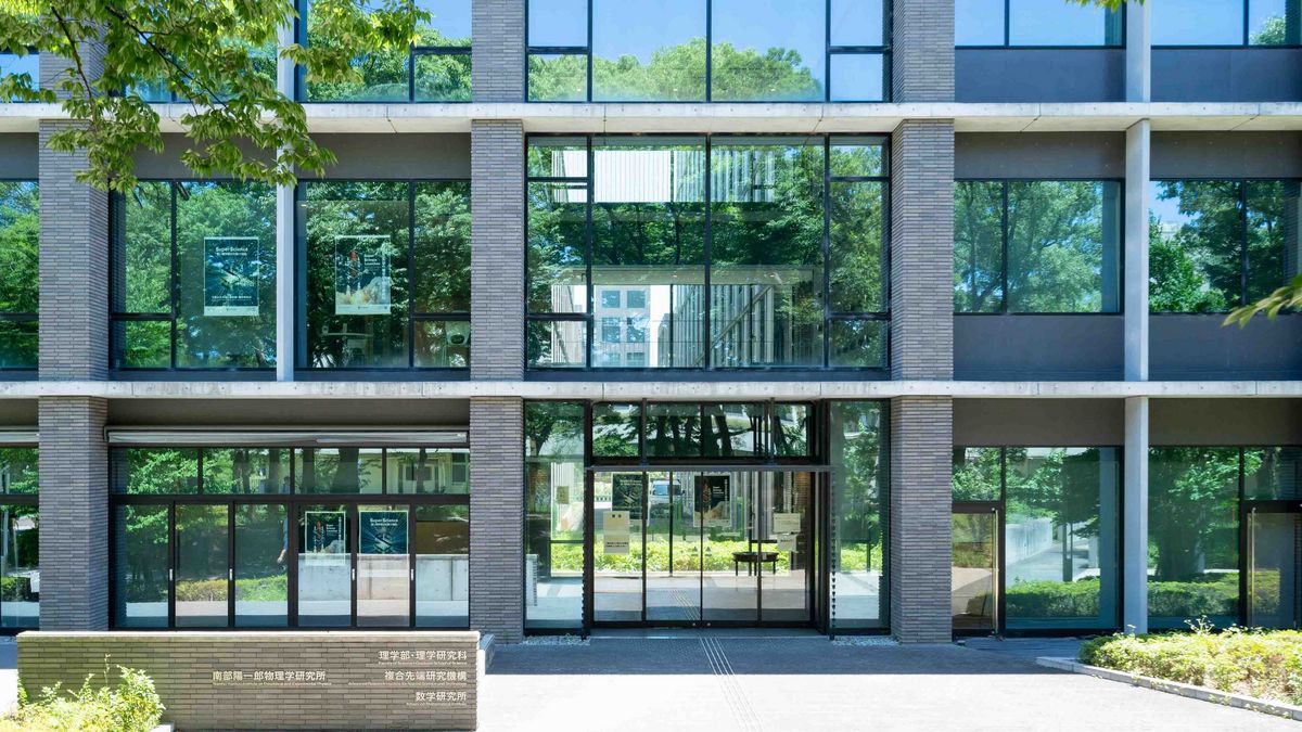 A modern Osaka Metropolitan University building with a grey façade and large windows, surrounded by greenery.