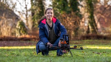 Eine Frau hockt auf einer Wiese, vor ihr ist eine Drohne platziert.