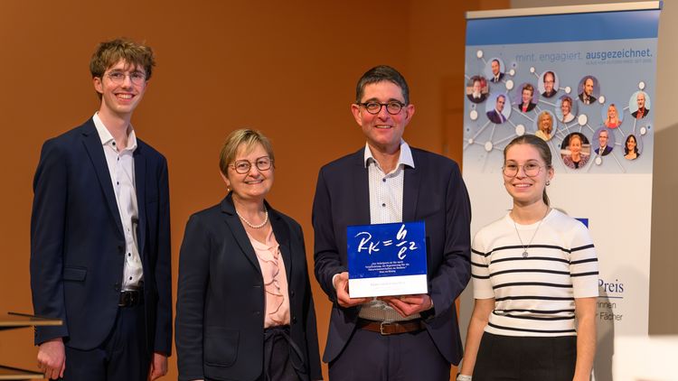 Four people are standing in front of an orange wall. They are wearing festive clothing. One of them is holding up an award. They are all smiling at the camera.
