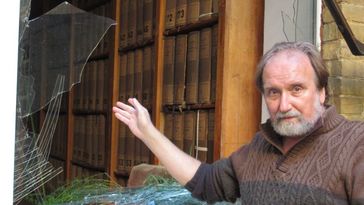 One of the men from the first picture is standing outside in front of a shattered window, in the background you can see the shelves with the old book spines again