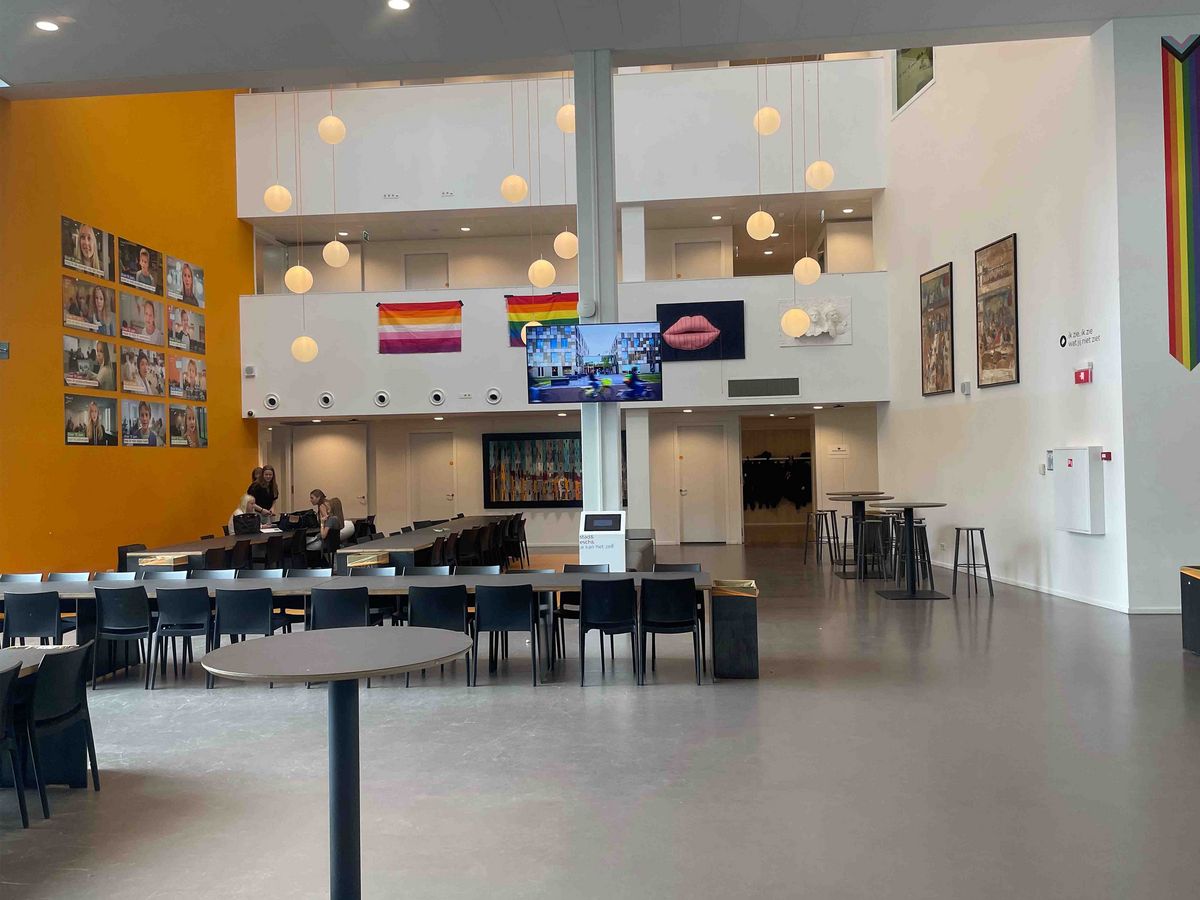 A large, light corridor in the Schule Stad&Esch with portraits, artworks and rainbow flags. A large screen with video in the center.