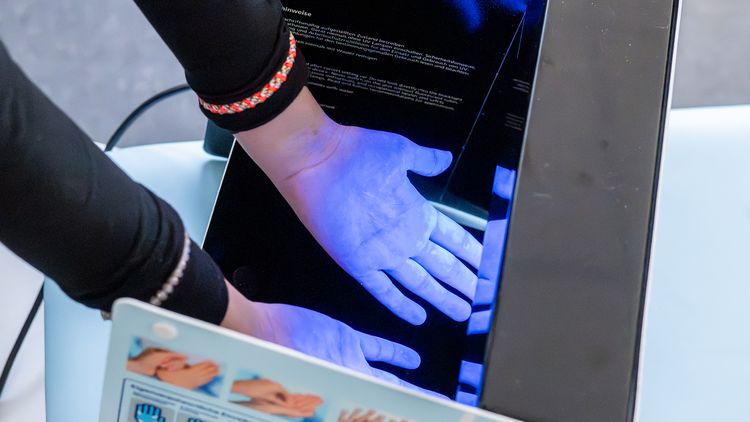 Hände unter Schwarzlichtlampe sollen Verunreinigungen deutlich machen.