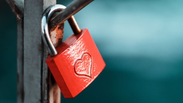 A red love lock with an engraved heart hangs on a fence.