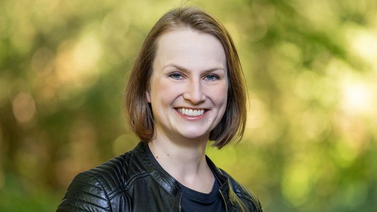 The picture shows Katharina Pöppel. She smiles at the camera. Trees can be seen in the background.