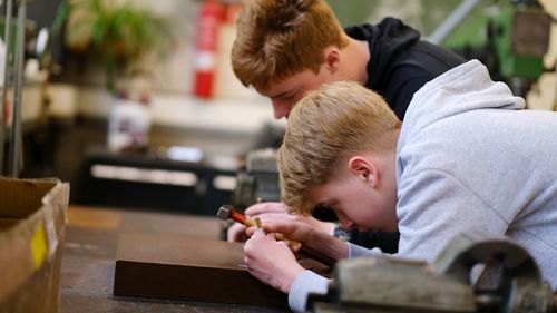 Two boys are working in a workshop. One of them is holding a hammer.