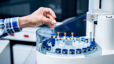 Close-up of a hand inserting a glass tube into a kind of rondel. There are several more tubes inside.