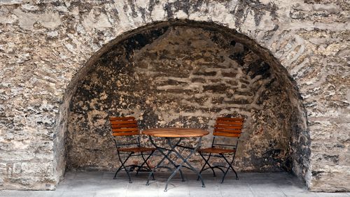 table, chairs, cafe, outdoors, restaurant, wall, stone, dining, sidewalk, nobody, diner, old, wood, horizontal, furniture, brown, structure, textured, rustic, patio, design, two, exterior, empty, brick, seats, bar, cafeteria, day, gray, city, old-fashioned, limestone, niche, recess, foldable, arch, architecture, alcove, medieval, castle, stronghold, ancient, weathered, fold, folding, yard, court, courtyard