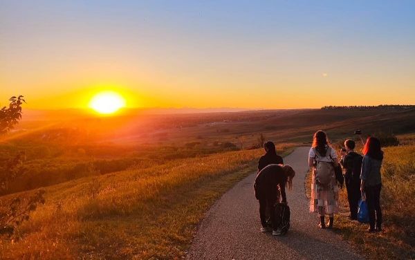Gruppe von Menschen spaziert bei Sonnenuntergang auf einem Weg durch offene Landschaft.