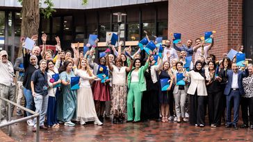 Eine Gruppe von Menschen vor der Mensagebäude der Uni Oldenburg. Sie halten Mappen in den Händen, einige recken diese nach oben. Die Menschen sehen fröhlich aus. 