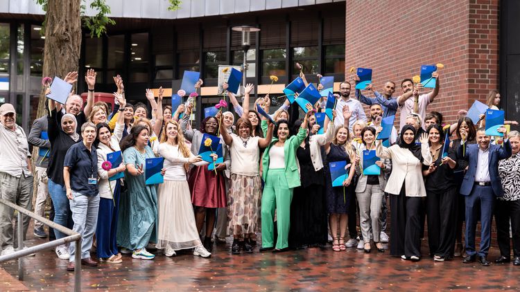 Eine Gruppe von Menschen vor der Mensagebäude der Uni Oldenburg. Sie halten Mappen in den Händen, einige recken diese nach oben. Die Menschen sehen fröhlich aus. 