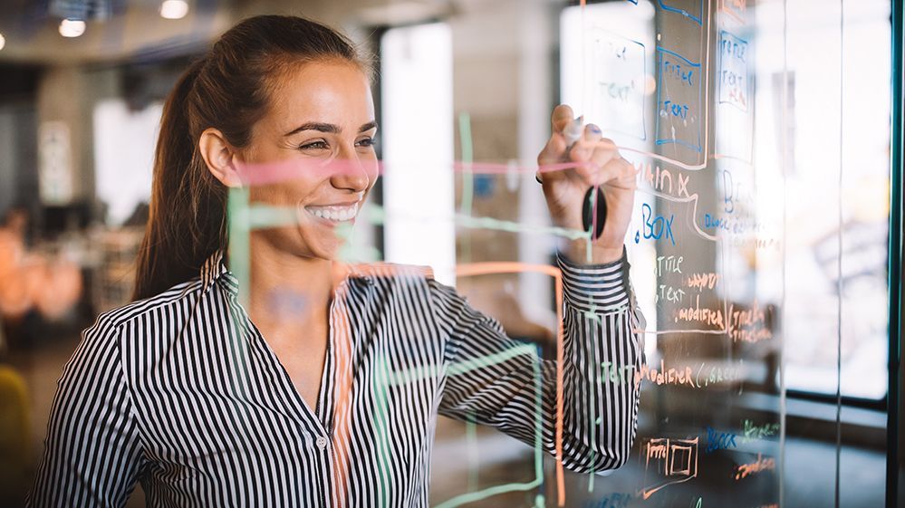 Glückliche Frau arbeitet und schreibt an einem Glasboard im Büro.