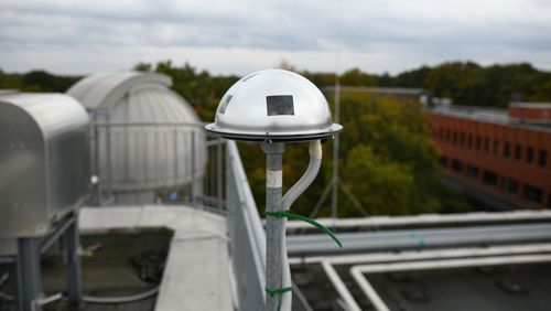 The camera is a dome-shaped metal part with some openings. It is located on a pole on the roof of a building, with the dome of the observatory in the background.