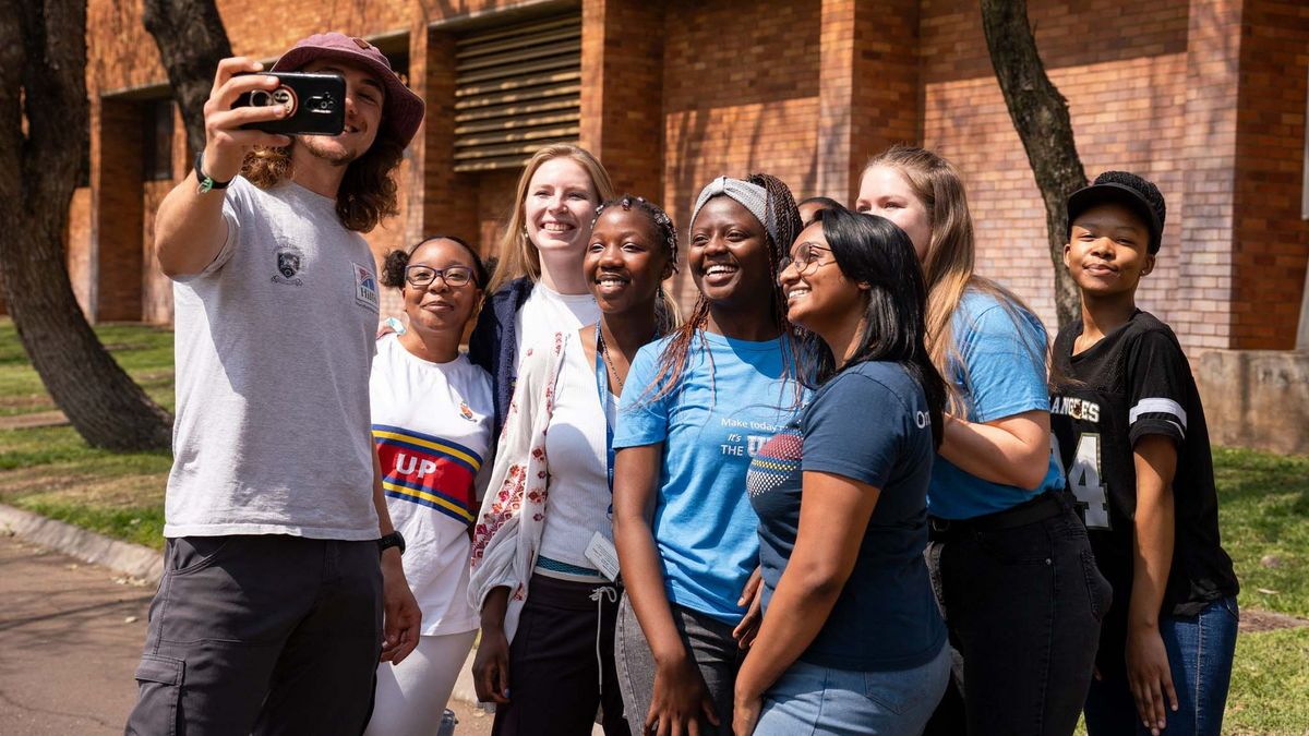Neun Studierende machen auf dem Campus der University of Pretoria ein Selfie. Sie lächeln und tragen teilweise Kleidung mit Uni-Logo.