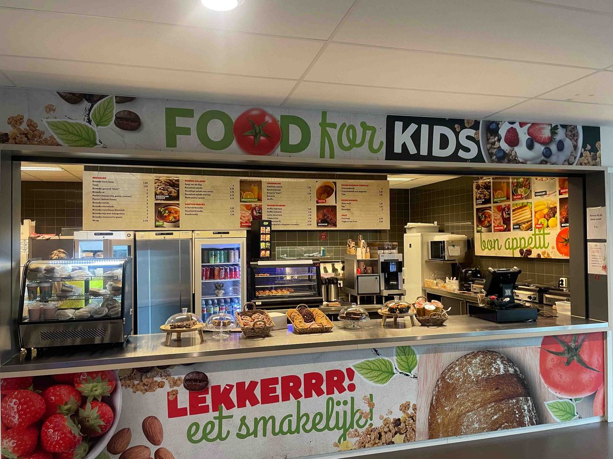 A school cafeteria with a menu "FOOD for KIDS" and food. "LEKKERRR! eet smakelijk!" is written on a sign.
