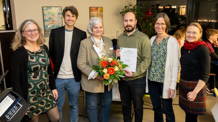 Das Bild zeigt die sechs Genannten. Sie stehen im Interkulturellen Treff und lächeln in die Kamera. Der Preisträger hält eine Urkunde, Frau Al-Shamery einen Blumenstrauß in den Händen.