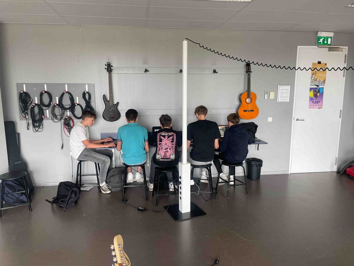 A room in the Schule Stad&Esch, where five students sit at notebooks and work. The room is equipped with guitars and cables.