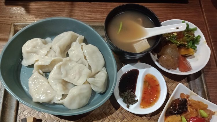 A tray with several plates and small bowls filled with dumplings, a soup, sauces and other side dishes.