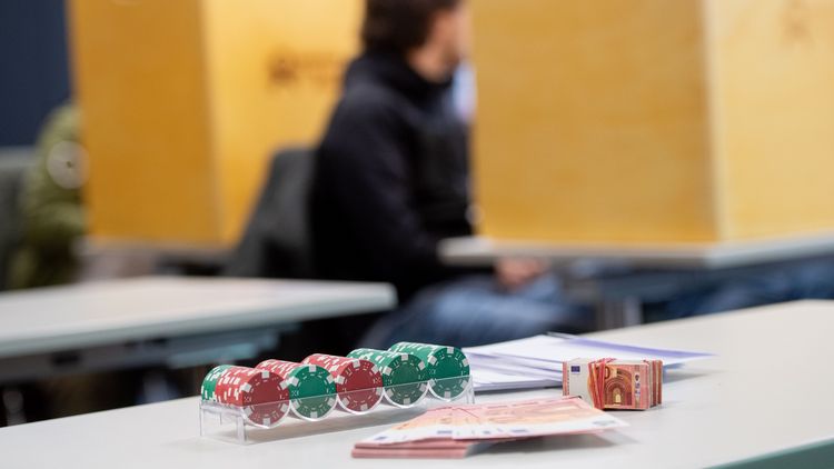 Auf dem Bild sind einige Pokerchips und Spielgeld zu sehen, im Hintergrund ein Studierender. 