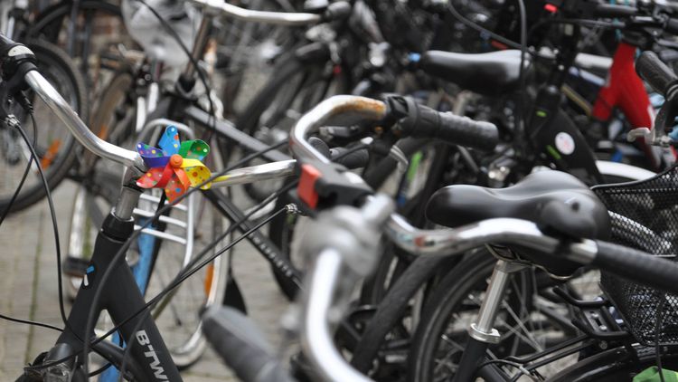 The picture shows a group of bicycles parked outside. One of the bikes has a small colourful wind chime on the front of the handlebars.