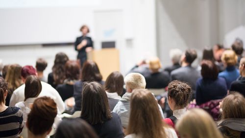 A woman stands in a lecture hall and gives a presentation.