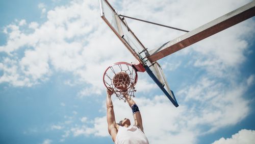 Junger Mensch, der am Basketballkorb per Slam-Dunk punktet