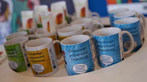 Some porcelain mugs with GIZ motifs stand on a white tray.
