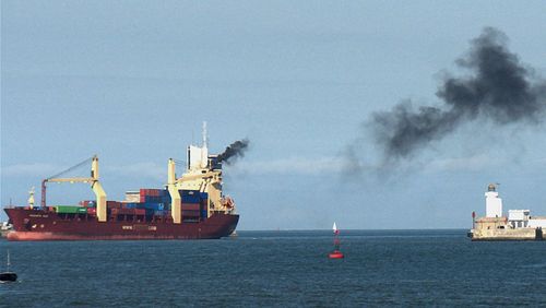 Cargo vessel emitting black exhaust gases to the air.