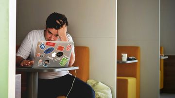 Man sits in front of open laptop and supports his head in his hand