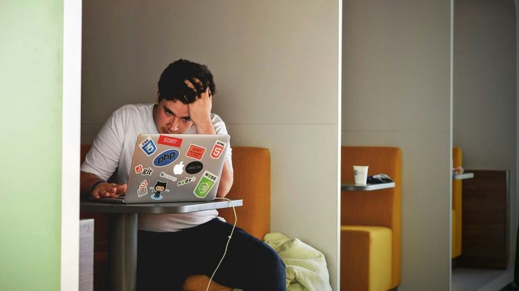 Mann sitzt vor geöffnetem Laptop und stützt seinen Kopf in der Hand