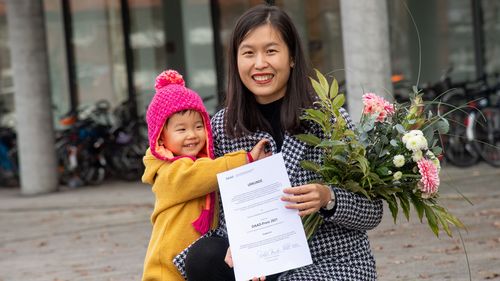Jingjing Xu mit Blumenstrauß, Urkunde und ihrer kleinen Tochter.