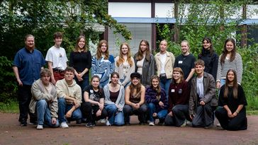 The picture shows 19 of the 22 volunteers who have lined up for a group photo. They are standing in front of a university building and smiling at the camera.