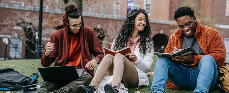 Three students are working on their assignments in front of a university building.