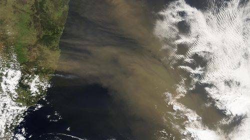 A satellite image shows the Australian coast, the Pacific Ocean, some white clouds and the brownish dust cloud.