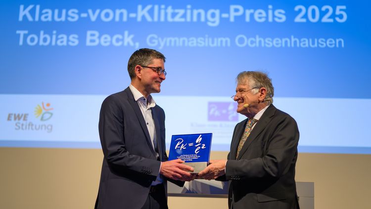 A middle-aged man receives an award from an elderly man. They smile at each other. They are wearing suits.