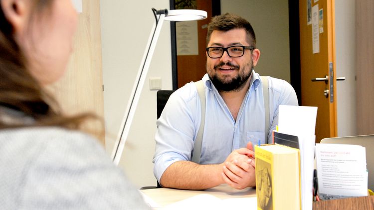 Max Bauer is sitting at a table with a student, in the foreground you can see some books.