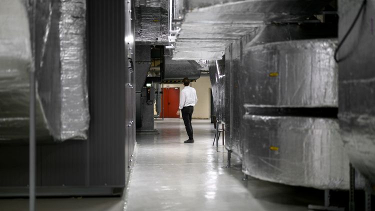 A person stands in a large room between the massive ventilation ducts, which are wrapped in shiny metallic insulation foil. 