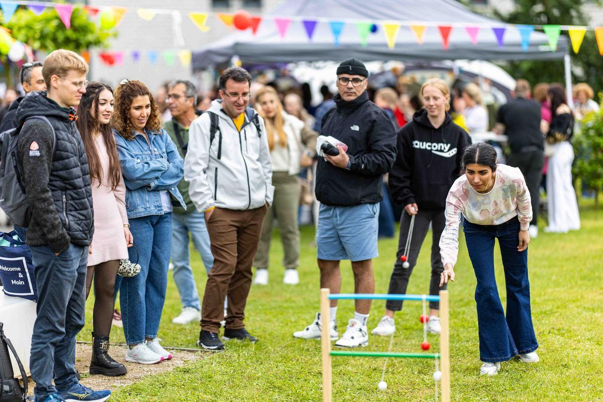 Leitergolf spielende Personen, die von weiteren Personen beobachtet werden.