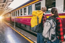 Das Foto zeigt einen jungen Mann und eine junge Frau mit Rucksacken, die an einem Bahnhof in einen rot-weißen Zug einsteigen.