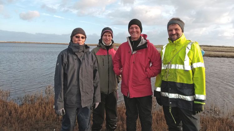 The four researchers in winter clothes in front of the Wadden Sea. 