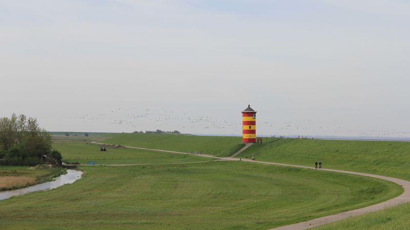 Der Pilsumer Leuchtturm, ein runder, elf Meter hoher, rot-gelb angestrichener Turm, liegt direkt auf dem Nordsee-Deich.