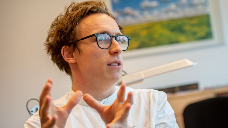Niklas Ellerich-Groppe in conversation. He gestures with his hands, wears glasses and a white shirt.