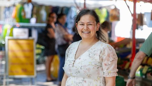 Junge Frau in sommerlicher Kleidung vor einem Marktstand.