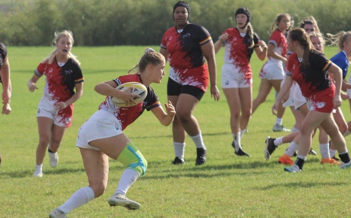 Rugby-Spielerinnen in Aktion auf einem grünen Rasenfeld.