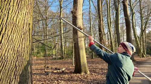 A young man holds a long pole in his hand. In front is a small disc that is to be attached to the tree.