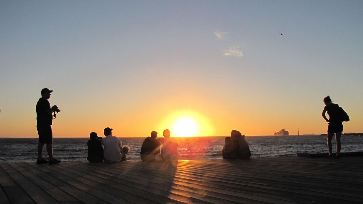 Menschen beobachten einen Sonnenuntergang am Meer mit orangefarbenem Himmel.