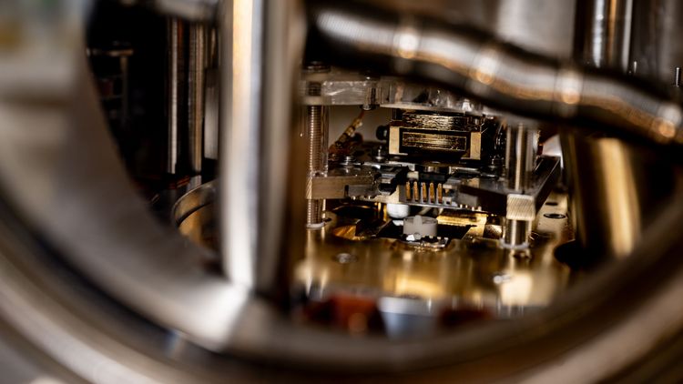 Das Bild zeigt ein Wärmemikroskop, das sich innerhalb einer Vakuumkammer befindet. Im Gegensatz zu der großen Messapparatur aus massivem Metall besteht das eigentliche Mikroskop aus kleinen, eher fragilen Bauteilen. Der Blick ist durch Metallstäbe im Vordergrund teils verdeckt. 