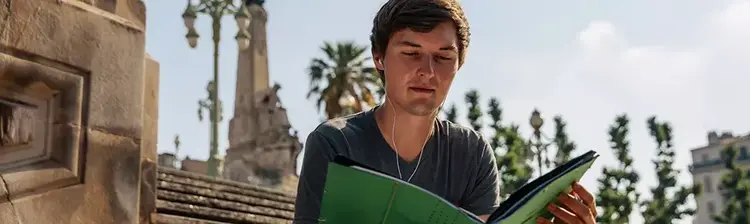 Ein junger Mann liest auf einer steinernen Treppe vor historischen Gebäuden.