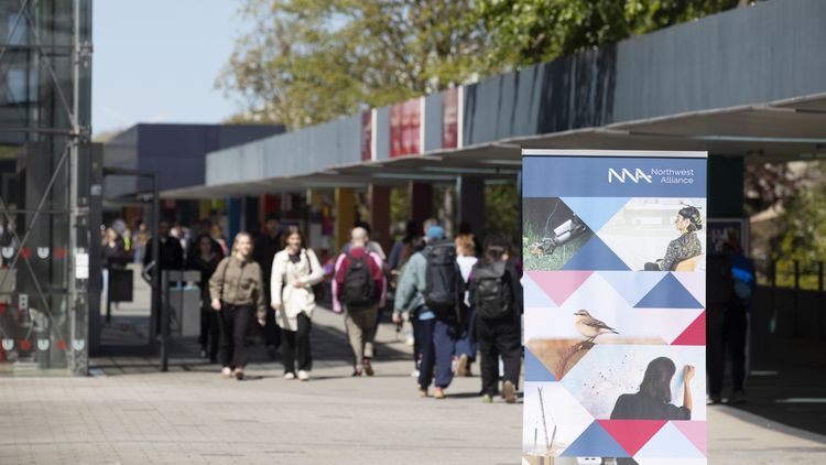  A group of people are walking along Bremen’s Uni-Boulevard; in the foreground, a display stand belonging to the Northwest Alliance can be seen. 